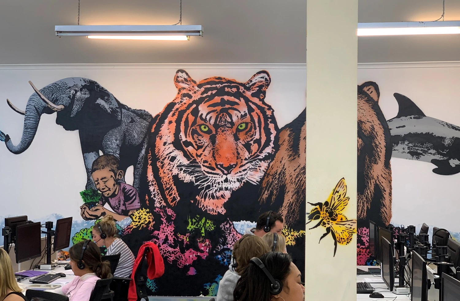 GiveTel team working in front of the animal mural on the call-centre floor